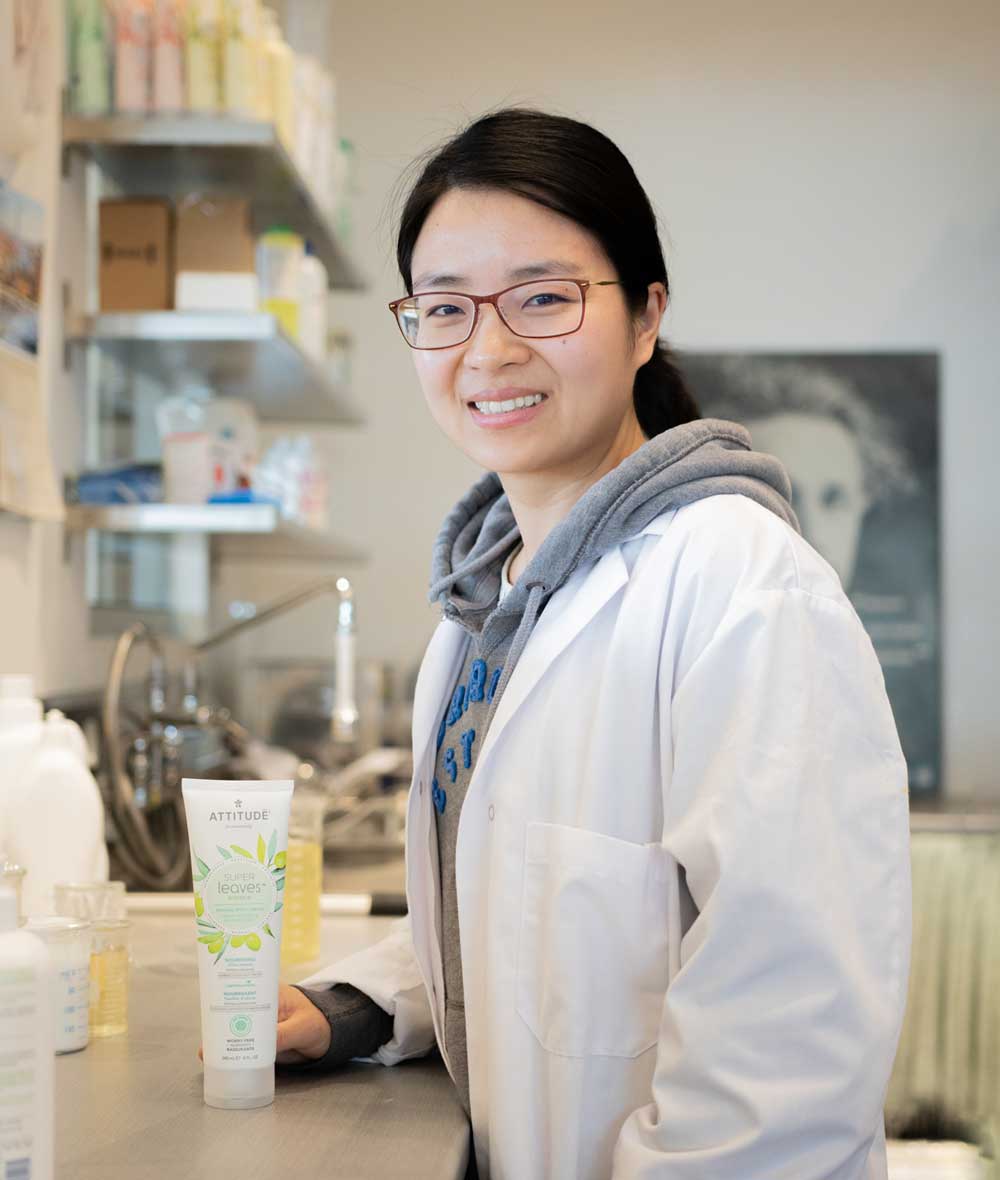 Femme souriante se tenant à côté de la crème pour le corps nourrissante Super Leaves ATTITUDE_fr? ALL_VARIANTS