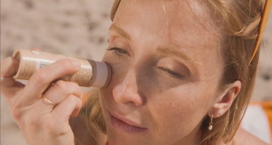 Femme à la plage appliquant sa crème solaire teinté en bâton ATTITUDE dans un emballage sans plastique fait de carton biodégradable